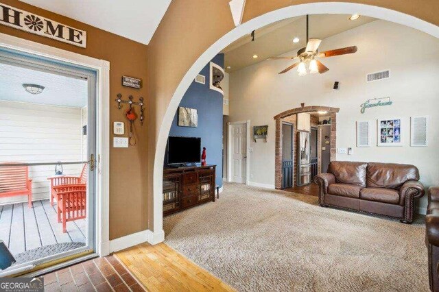 living room with hardwood / wood-style flooring, ceiling fan, and high vaulted ceiling