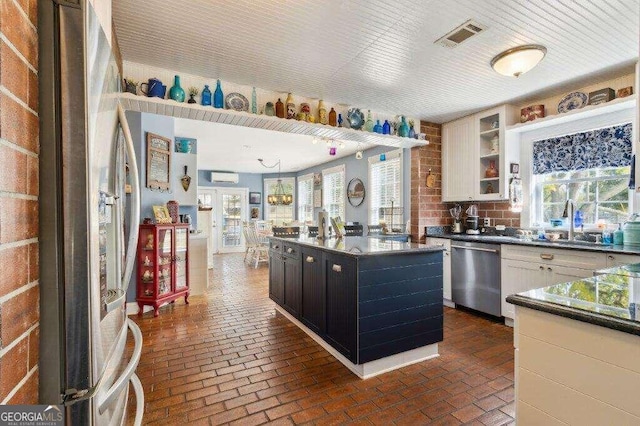 kitchen featuring appliances with stainless steel finishes, a wall mounted air conditioner, white cabinetry, brick wall, and a center island with sink