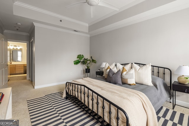 carpeted bedroom with crown molding, a raised ceiling, ensuite bath, and ceiling fan