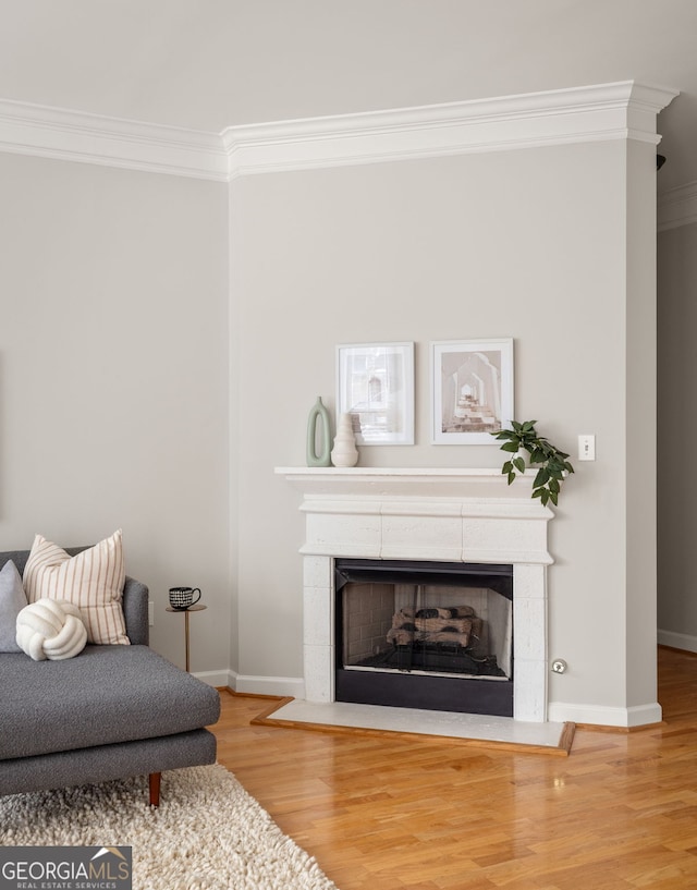 living area featuring a tiled fireplace, crown molding, and wood-type flooring