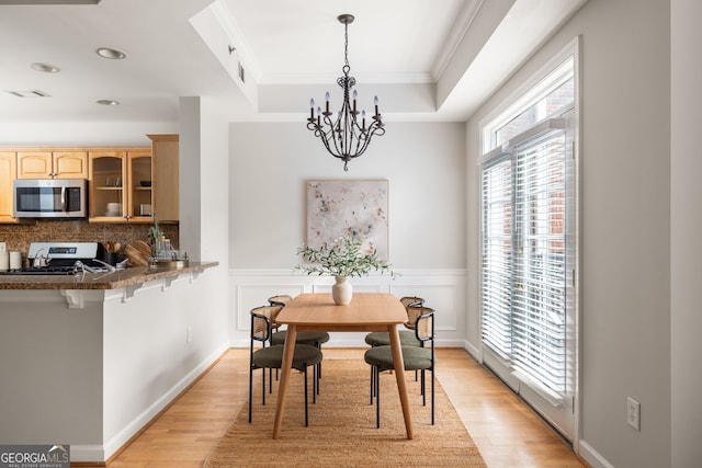 dining room featuring a tray ceiling, ornamental molding, an inviting chandelier, and light wood-type flooring