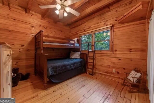 bedroom featuring wood walls, beam ceiling, light wood-type flooring, and ceiling fan