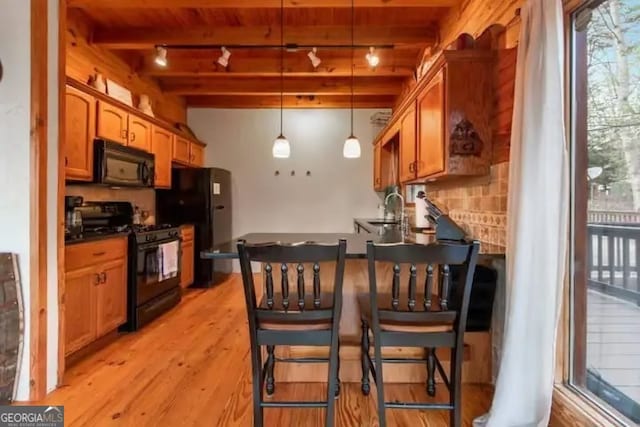 kitchen featuring black appliances, track lighting, pendant lighting, beam ceiling, and light hardwood / wood-style flooring