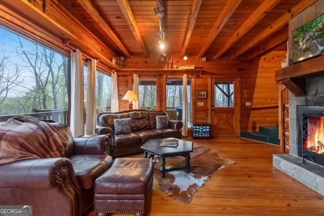 living room featuring beamed ceiling, wooden walls, a fireplace, and light wood-type flooring