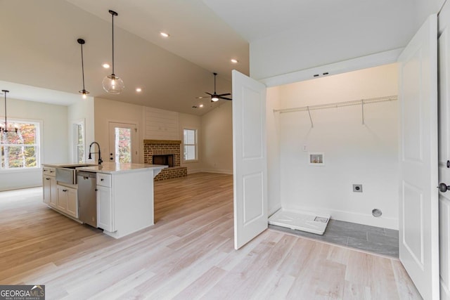 kitchen featuring light hardwood / wood-style flooring, decorative light fixtures, a kitchen island with sink, and stainless steel dishwasher