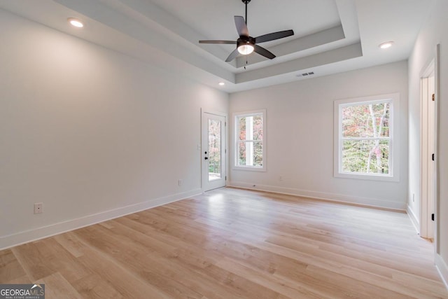 empty room with a tray ceiling, light wood-type flooring, and ceiling fan