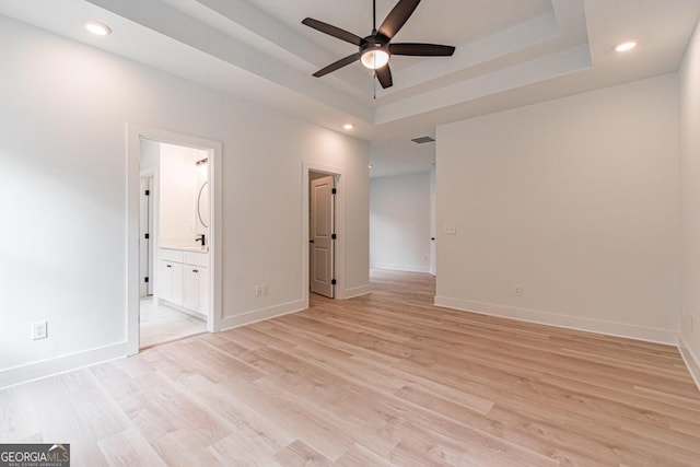 unfurnished bedroom featuring ensuite bath, a tray ceiling, and light hardwood / wood-style floors