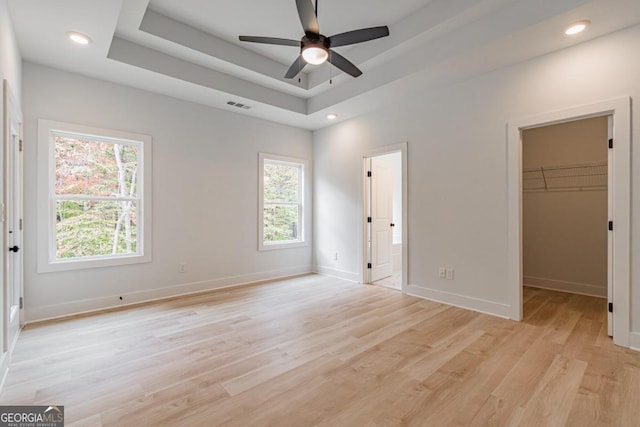 unfurnished bedroom with a spacious closet, multiple windows, a closet, and ceiling fan