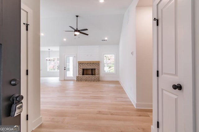 unfurnished living room with lofted ceiling, light hardwood / wood-style flooring, a fireplace, and ceiling fan with notable chandelier