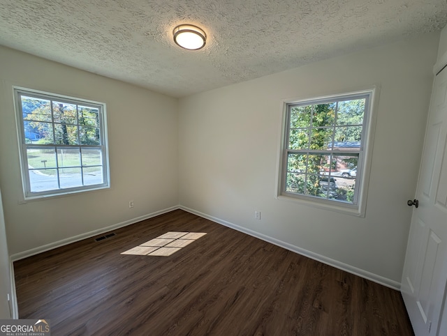 empty room with a textured ceiling, dark hardwood / wood-style floors, and a healthy amount of sunlight