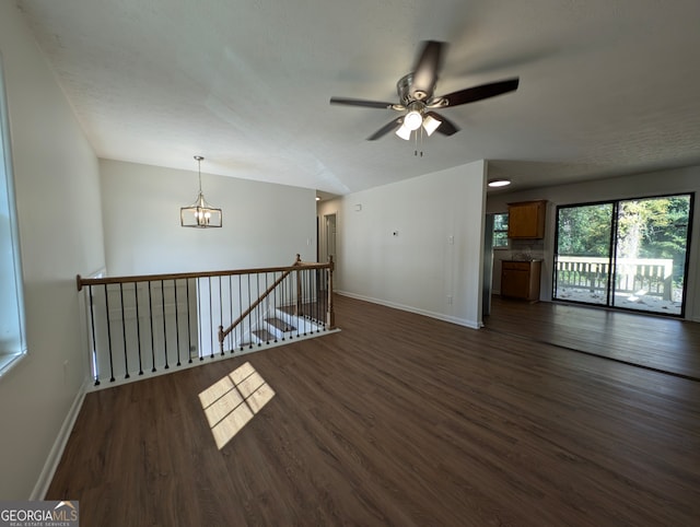 spare room with a textured ceiling, ceiling fan with notable chandelier, and dark wood-type flooring