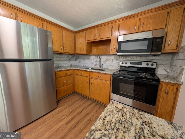 kitchen with sink, light stone counters, light hardwood / wood-style floors, a textured ceiling, and appliances with stainless steel finishes