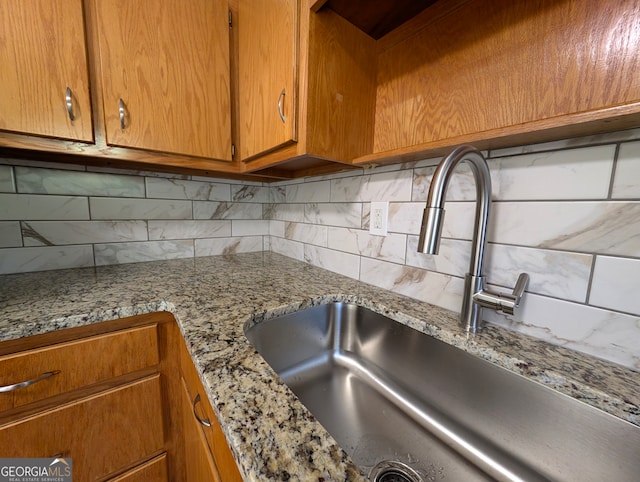 kitchen featuring light stone countertops, backsplash, and sink