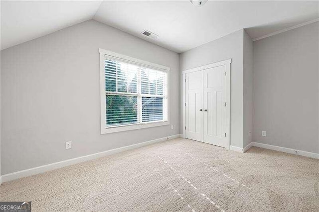 unfurnished bedroom with vaulted ceiling, light colored carpet, and a closet