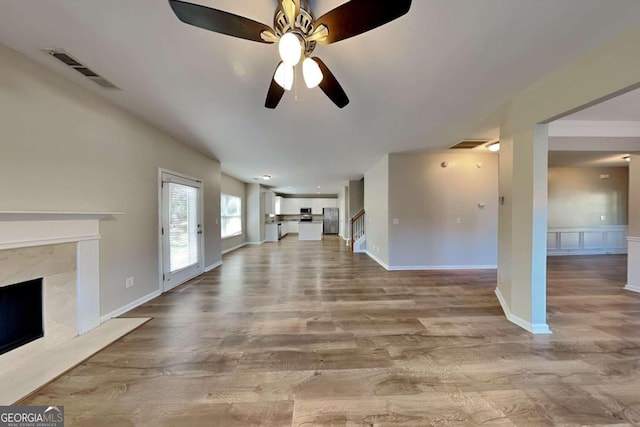 unfurnished living room with a premium fireplace, light wood-type flooring, and ceiling fan