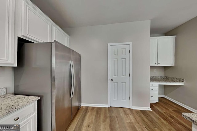 kitchen with built in desk, white cabinetry, light stone counters, light hardwood / wood-style floors, and stainless steel refrigerator