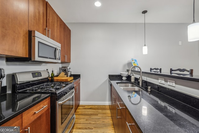 kitchen featuring appliances with stainless steel finishes, sink, decorative light fixtures, light wood-type flooring, and dark stone counters