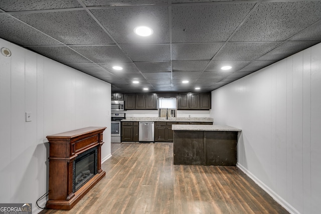 kitchen featuring appliances with stainless steel finishes, a paneled ceiling, dark brown cabinetry, wooden walls, and dark hardwood / wood-style floors