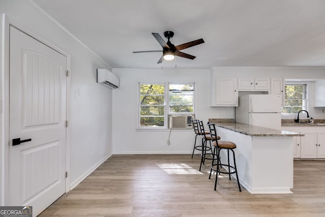 kitchen featuring an AC wall unit, a kitchen breakfast bar, light stone countertops, white refrigerator, and white cabinetry