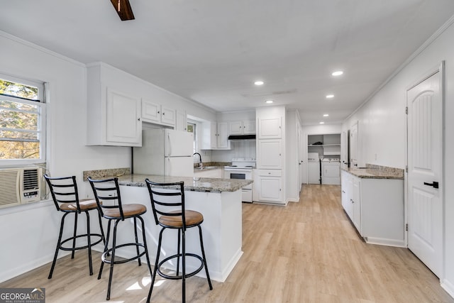 kitchen featuring white appliances, kitchen peninsula, a breakfast bar area, white cabinetry, and light hardwood / wood-style flooring