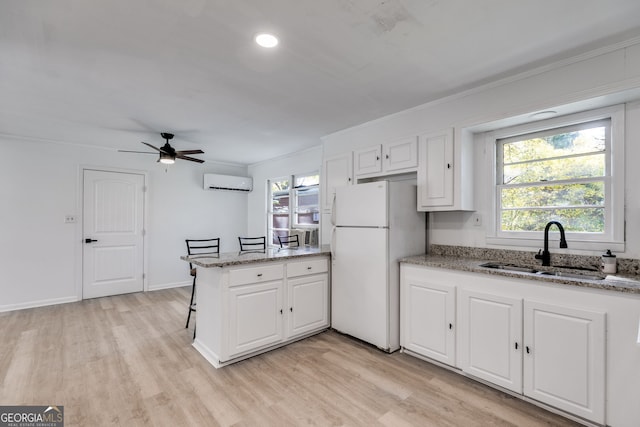 kitchen featuring a wall mounted AC, sink, white refrigerator, white cabinetry, and light stone counters