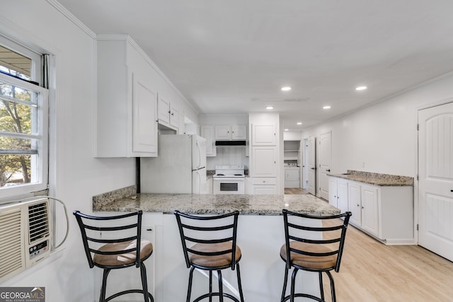 kitchen featuring kitchen peninsula, white cabinets, a breakfast bar area, light wood-type flooring, and white appliances