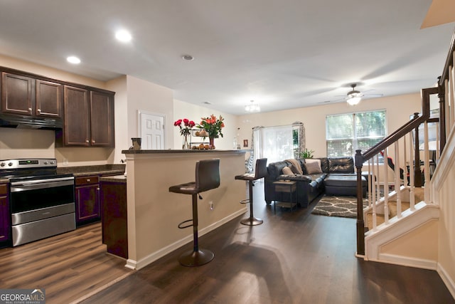 kitchen with dark brown cabinetry, dark hardwood / wood-style floors, ceiling fan, a breakfast bar, and stainless steel electric stove