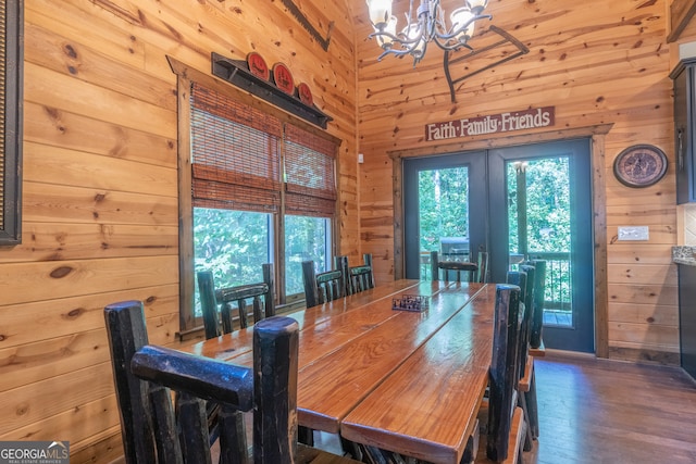 dining space featuring french doors, wood walls, a chandelier, and dark wood-type flooring