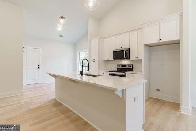 kitchen with light stone countertops, sink, white cabinetry, stainless steel appliances, and a kitchen island with sink