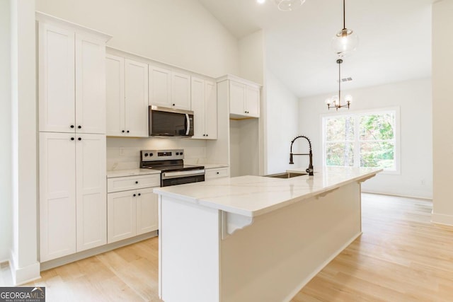 kitchen featuring appliances with stainless steel finishes, decorative light fixtures, white cabinetry, and an island with sink