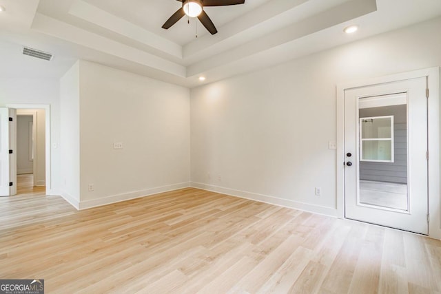 empty room featuring ceiling fan, a tray ceiling, and light hardwood / wood-style flooring