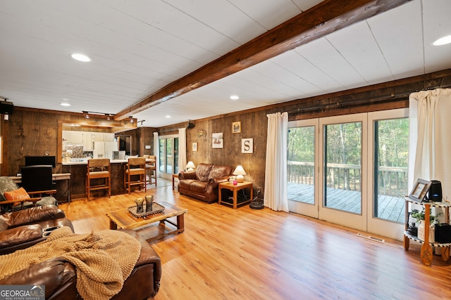 living room featuring light hardwood / wood-style flooring, wood walls, and beamed ceiling