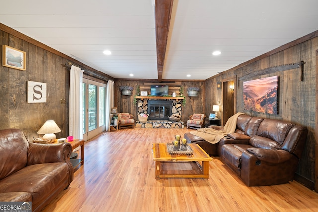 living room featuring beam ceiling, wooden walls, light hardwood / wood-style flooring, and a stone fireplace