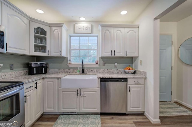 kitchen featuring appliances with stainless steel finishes, white cabinetry, wood-type flooring, sink, and light stone counters