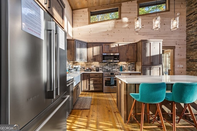 kitchen featuring wood walls, light hardwood / wood-style floors, stainless steel appliances, dark brown cabinetry, and high vaulted ceiling