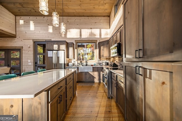 kitchen featuring wooden ceiling, high end appliances, a center island, pendant lighting, and wood walls