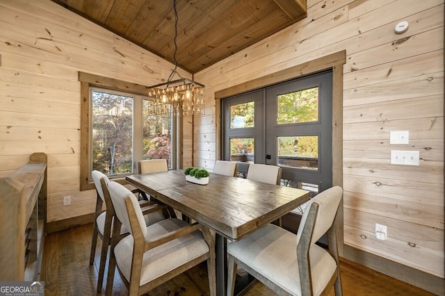 dining room with lofted ceiling, wood ceiling, dark wood-type flooring, wooden walls, and a chandelier