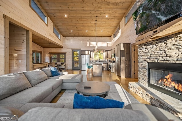 living room featuring a stone fireplace, wood-type flooring, a towering ceiling, and wood walls