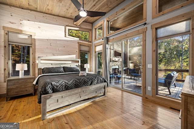 bedroom featuring access to outside, light hardwood / wood-style flooring, wood walls, and ceiling fan