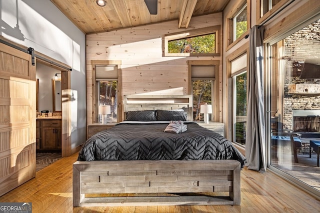 bedroom featuring a barn door, a fireplace, light wood-type flooring, and wooden ceiling