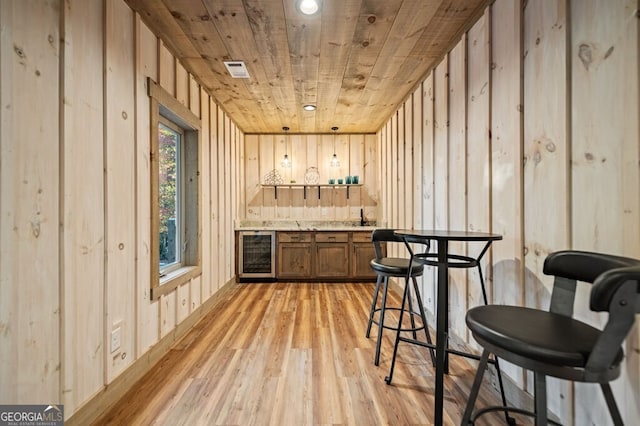 bar with wood ceiling, wooden walls, light hardwood / wood-style flooring, sink, and beverage cooler