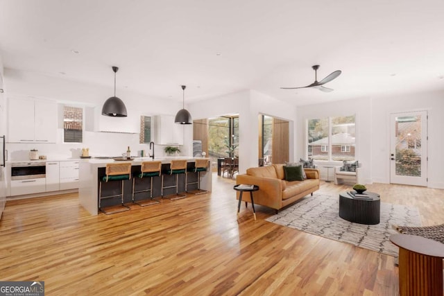 living room featuring ceiling fan, sink, and light wood-type flooring