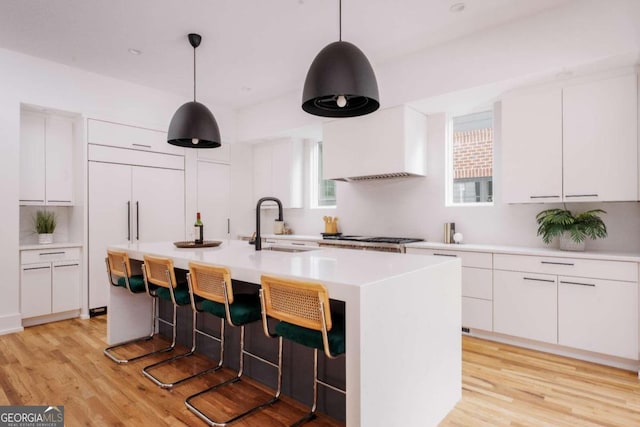 kitchen featuring sink, a kitchen island with sink, white cabinetry, light wood-type flooring, and decorative light fixtures