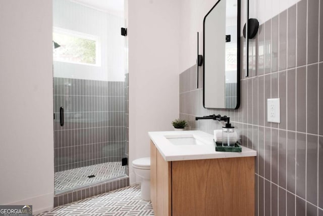 bathroom featuring a shower with shower door, vanity, toilet, and tile walls