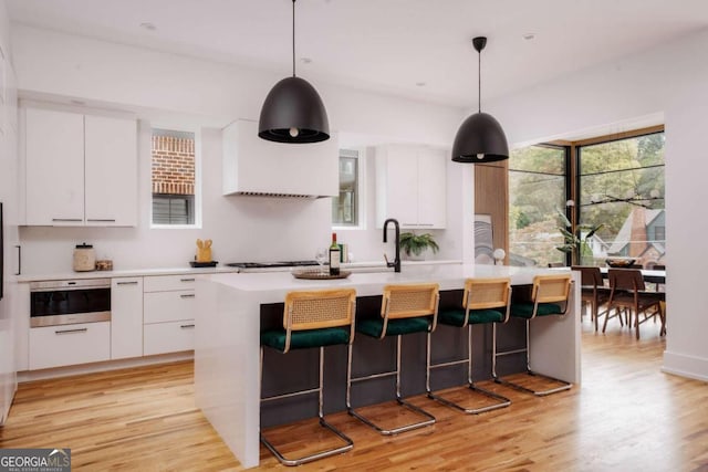 kitchen featuring pendant lighting, a center island with sink, light hardwood / wood-style flooring, and white cabinets