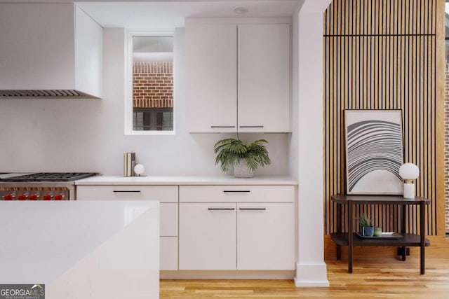 kitchen with white cabinets, light hardwood / wood-style floors, range hood, and stainless steel range oven