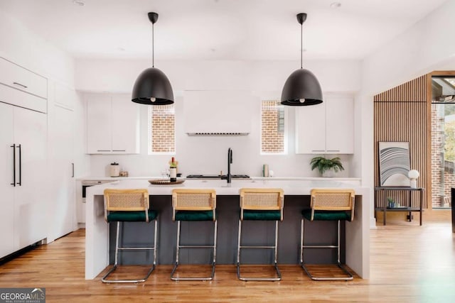 kitchen with hanging light fixtures, white cabinetry, a center island with sink, and light wood-type flooring