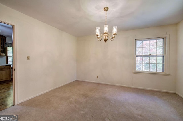 empty room with a notable chandelier, carpet flooring, and baseboards