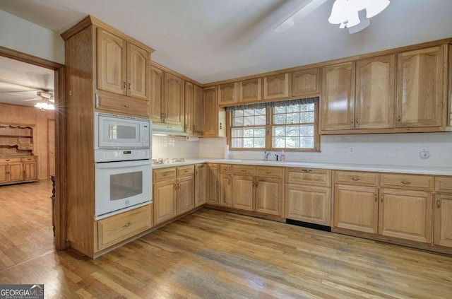 kitchen with white appliances, tasteful backsplash, light wood finished floors, light countertops, and a sink