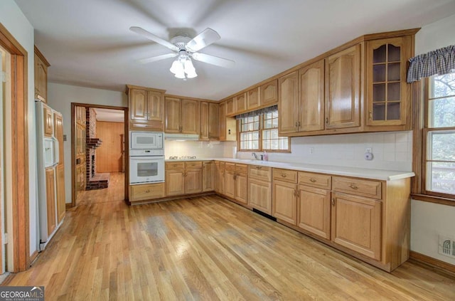 kitchen with light wood finished floors, light countertops, white appliances, and backsplash